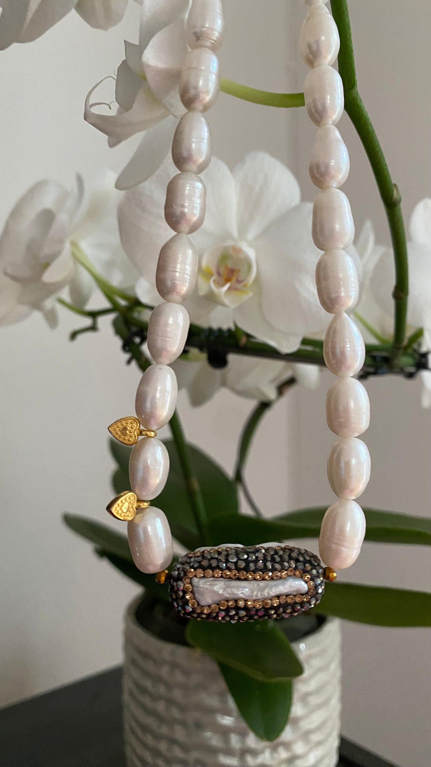 Nahaufnahme des ovalen Kristallanhängers mit weißen Süßwasserperlen und goldenen Akzenten.