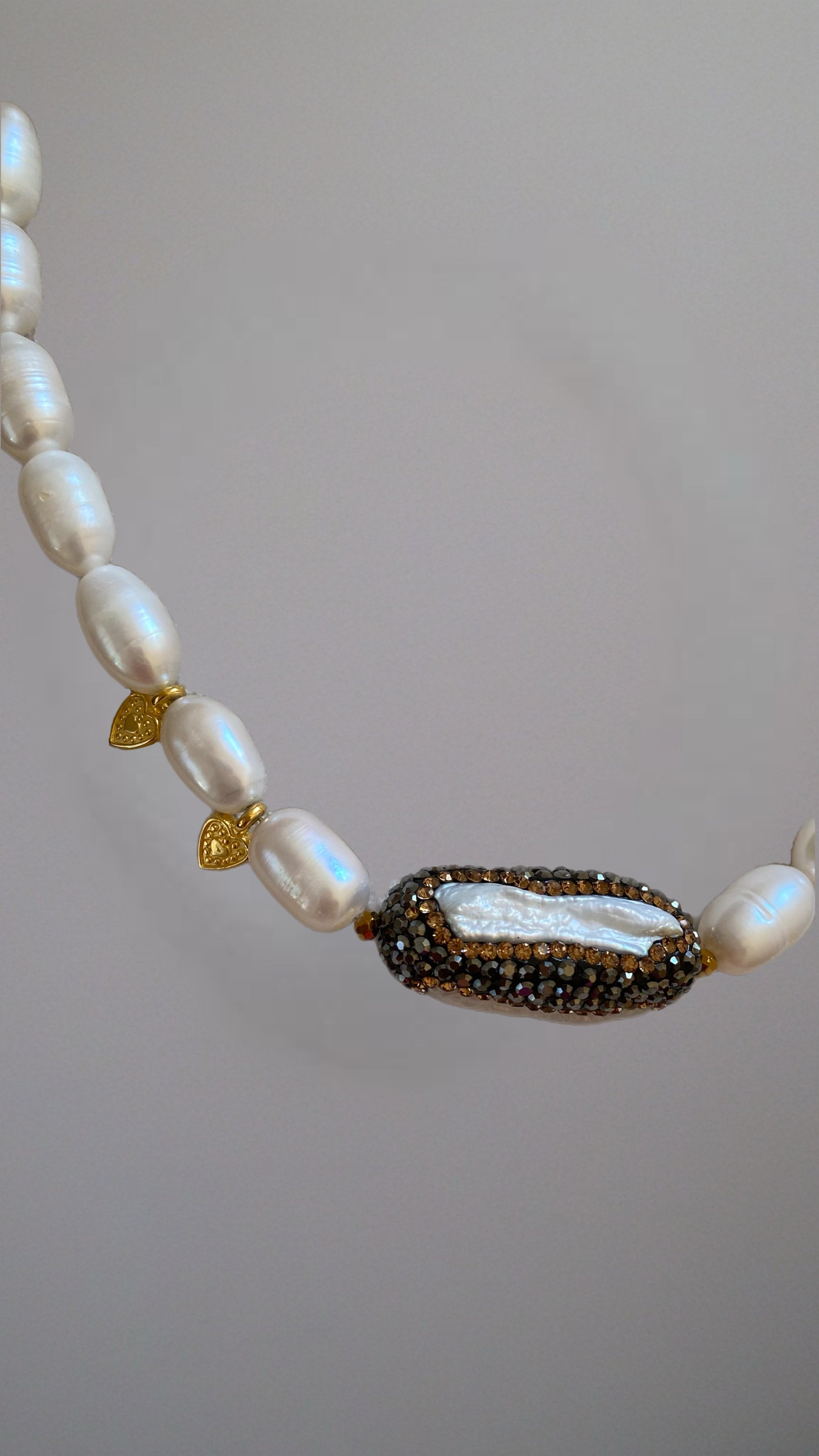 Nahaufnahme des ovalen Kristallanhängers mit weißen Süßwasserperlen und goldenen Akzenten.